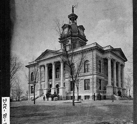 A stone courthouse in black and white with Greek columns and a dome.